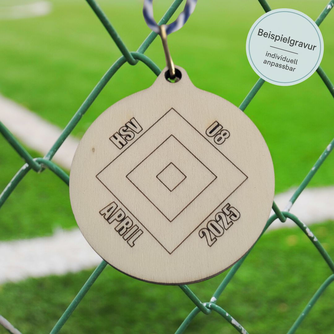 Medaille aus Holz hängt am Zaun eines Fußballplatzes, sie ist individuell gestaltet mit dem Namen und Logo des Vereins sowie des entsprechenden Turniers.