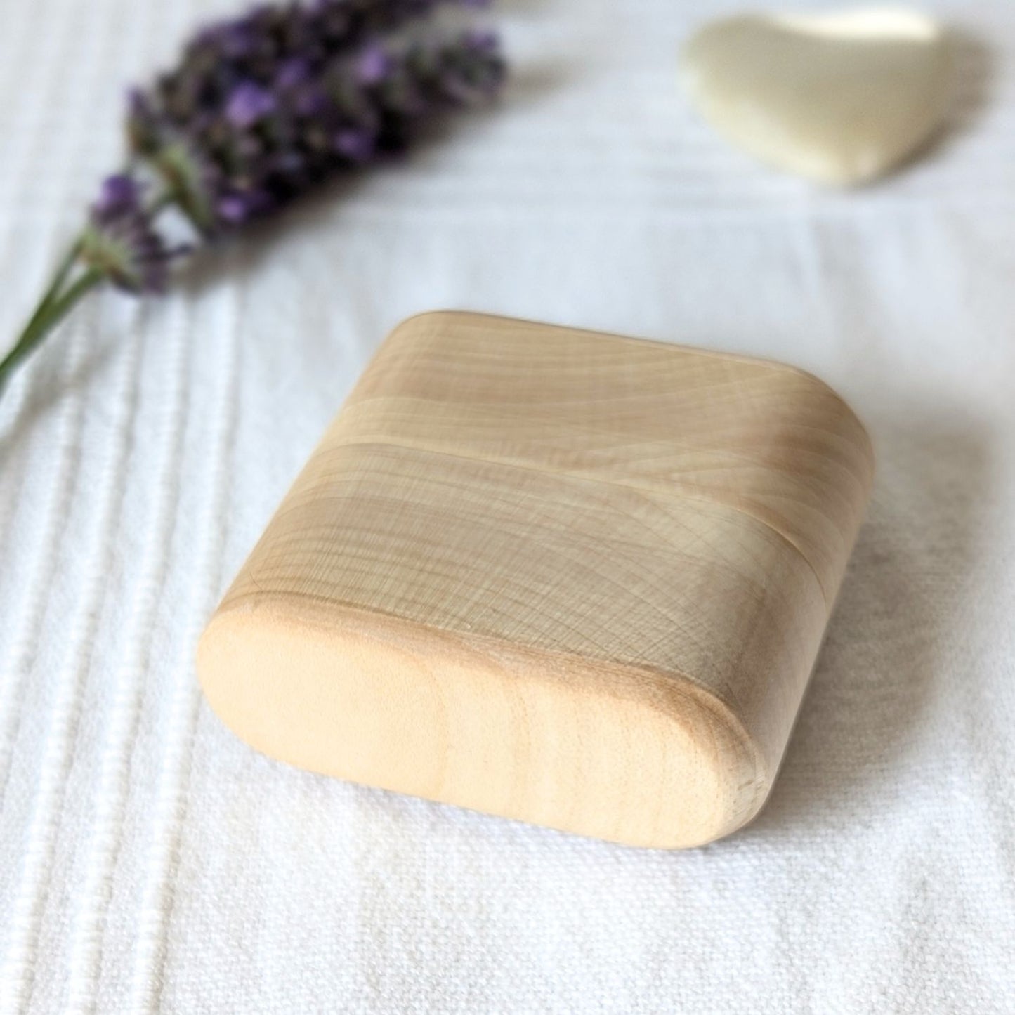 Geschlossene Tamponbox aus Ahornholz auf hellem Stoff, natürliche und sanfte Produktdarstellung.