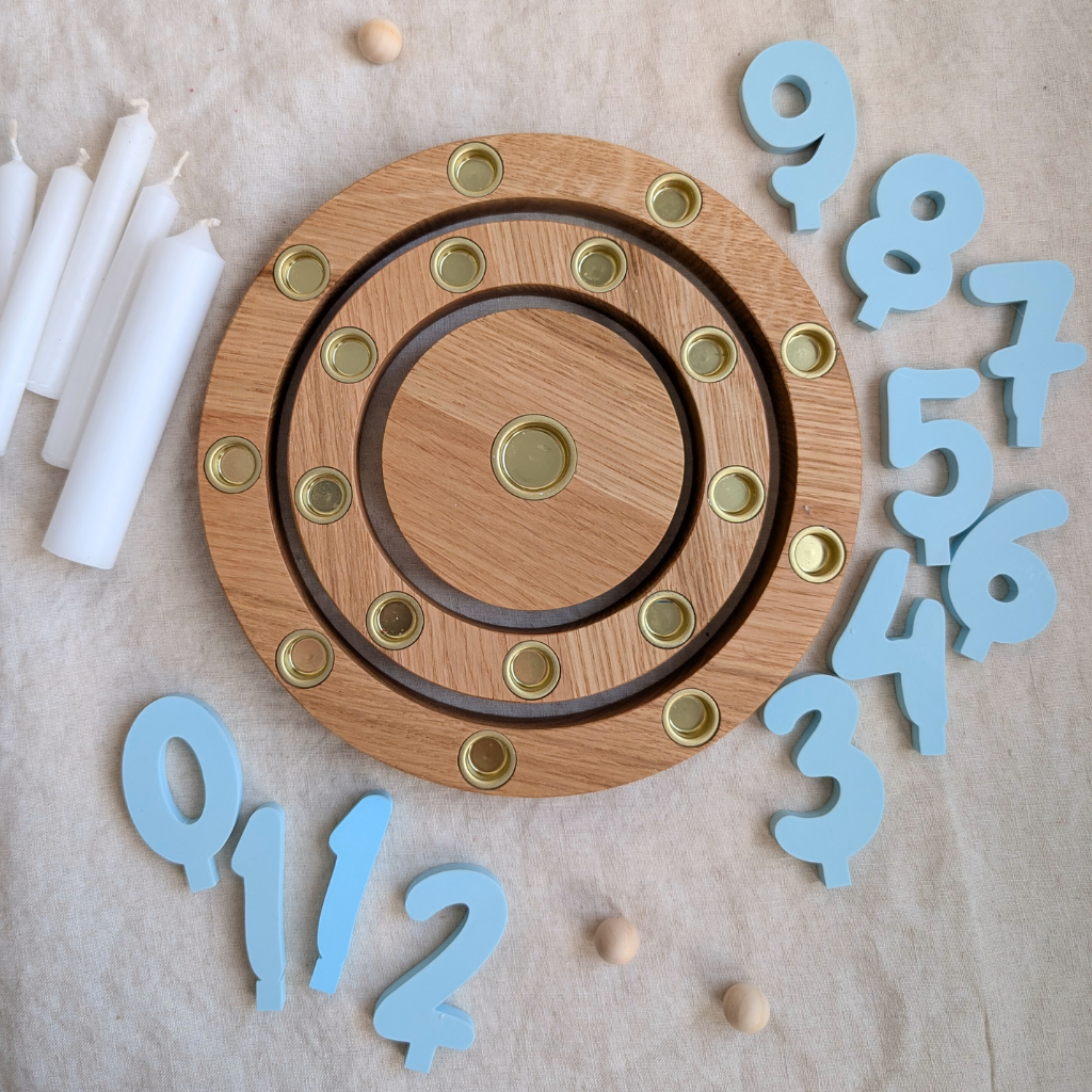 Geburtstagsring aus Eiche mit 18 Kerzenplätzen, weißen Kerzen und graublauen Zahlensteckern auf hellem Stoff