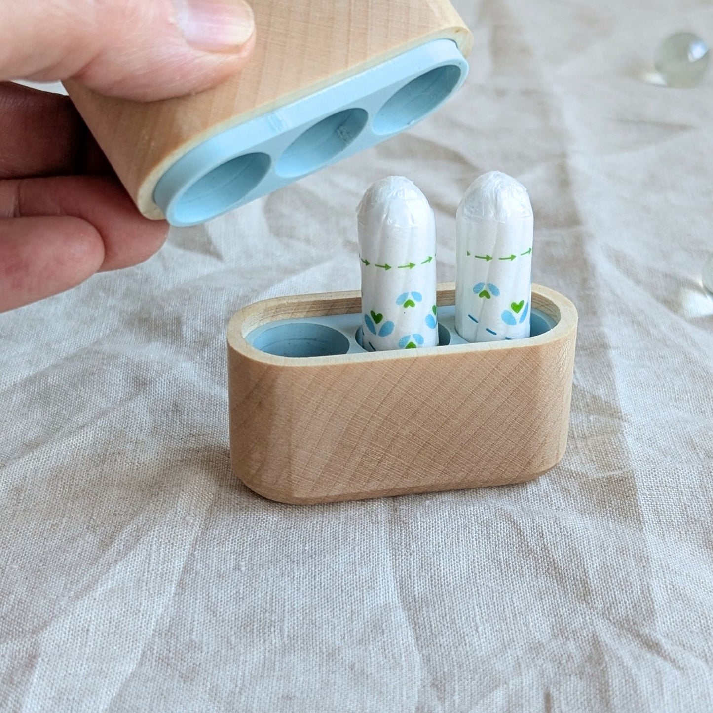 Geöffnete Tamponbox aus Ahornholz mit hellblauem Innenfach und zwei eingelegten Tampons