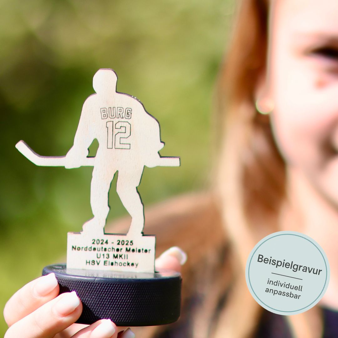 Ein Mädchen hält den gewonnenen Eishockey-Pokal aus Holz in die Kamera. Auf dem Pokal steht personalisiert der Name des Mädchens plus die Rückennummer.